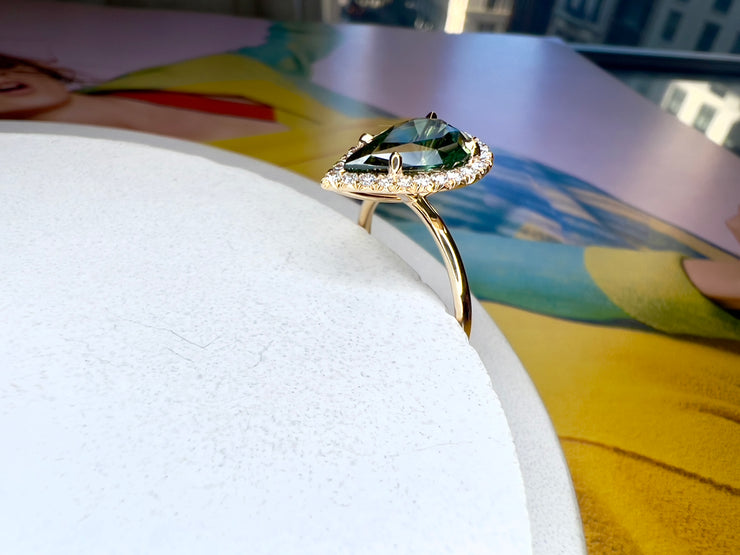 Lennox 3.04 carat natural green sapphire engagement ring seen from side profile with green pear shaped center stone and conflict free white diamond halo with thin dainty gold band and low setting 