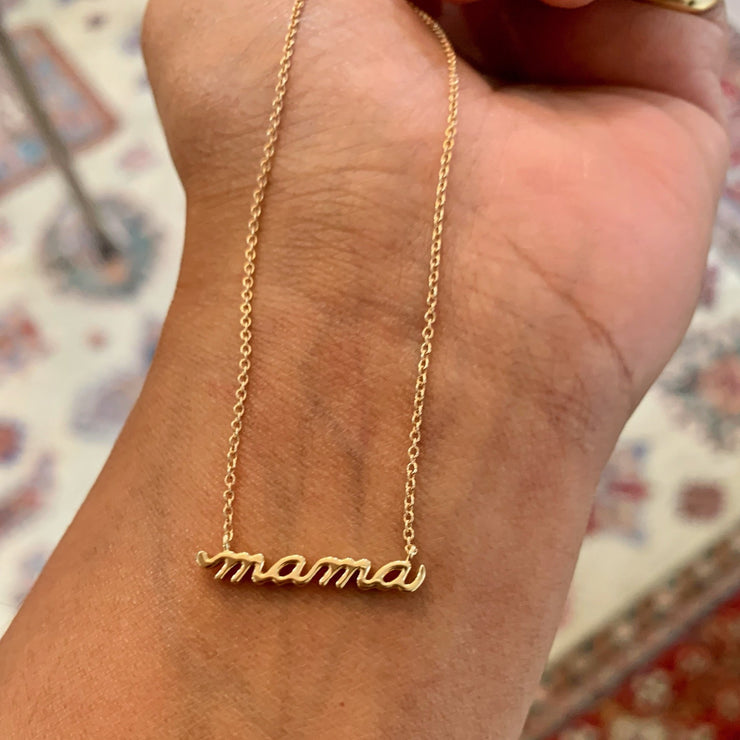 A 14k gold necklace that says MAMA in script. Handmade by DANA WALDEN JEWELRY NYC.