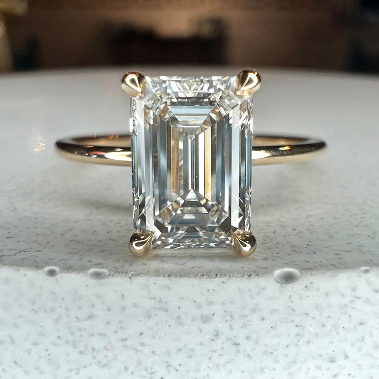 1.57 carat lab grown emerald cut engagement ring set in 14k yellow gold with ultra thin dainty band and hidden halo