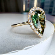 Lennox pear shaped green sapphire engagement ring from side profile with conflict free diamond halo and recycled 14k yellow gold with thin dainty 14k yellow gold by Dana Walden Bridal in NYC