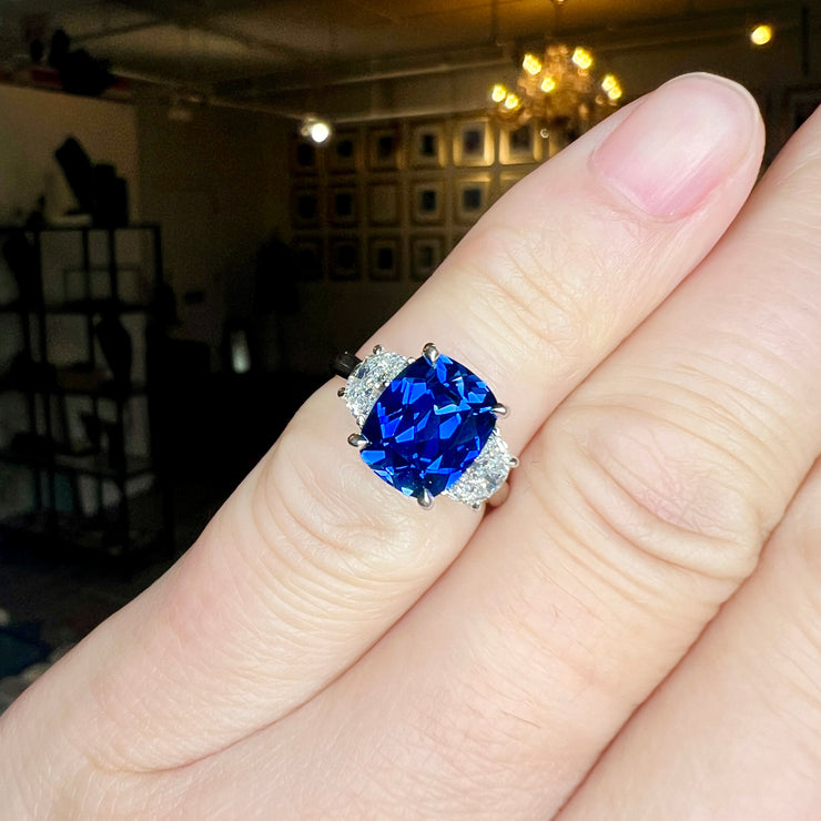 Unique Sapphire Alexandra lab sapphire engagement ring with half-moon, lunette diamonds shown on the hand in our NYC showroom. DANA WALDEN BRIDAL.