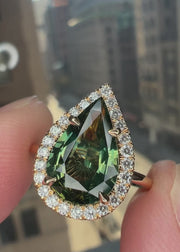 Video of Lennox natural green sapphire engagement ring in hand with 3.04 carat pear shaped sapphire in conflict-free white diamond halo with a thin dainty yellow gold band handmade in NYC by Dana Walden Bridal