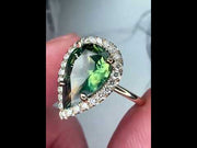 Video of Lennox natural green sapphire engagement ring in hand with 3.04 carat pear shaped sapphire in conflict-free white diamond halo with a thin dainty yellow gold band handmade in NYC by Dana Walden Bridal 