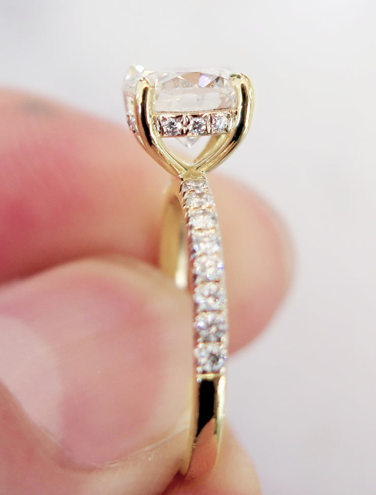 Side view of a Delicate diamond engagement ring in yellow gold with accent diamonds in the band and in a hidden halo under the center gemstone.