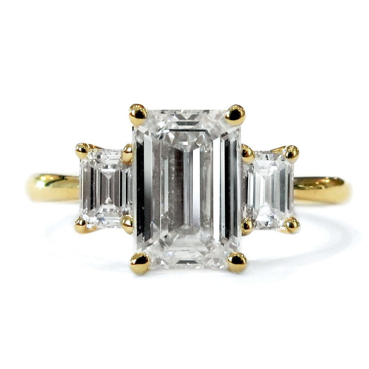 Classic 2 carat emerald cut three stone engagement ring in yellow gold with delicate band 