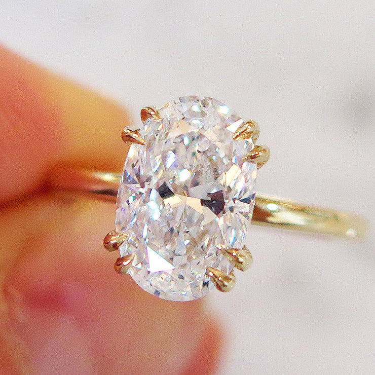 Oval diamond solitaire engagement ring, 2 carats, yellow gold setting, thin band, in hand