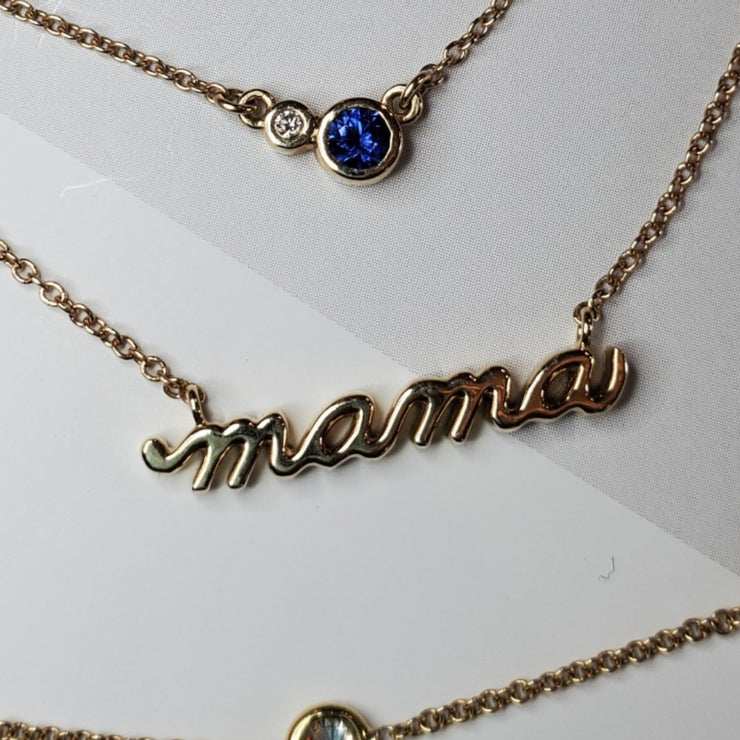 A 14k gold necklace that says MAMA in script. Handmade by DANA WALDEN JEWELRY NYC.