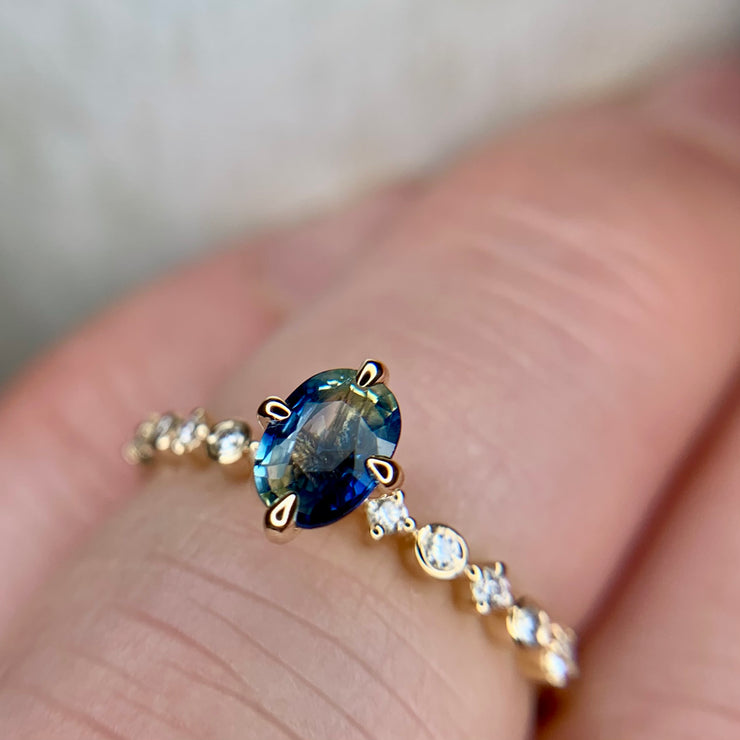 Blue green bicolor sapphire engagement ring with teal hues in yellow gold & diamond band on hand by Dana Walden Bridal NYC