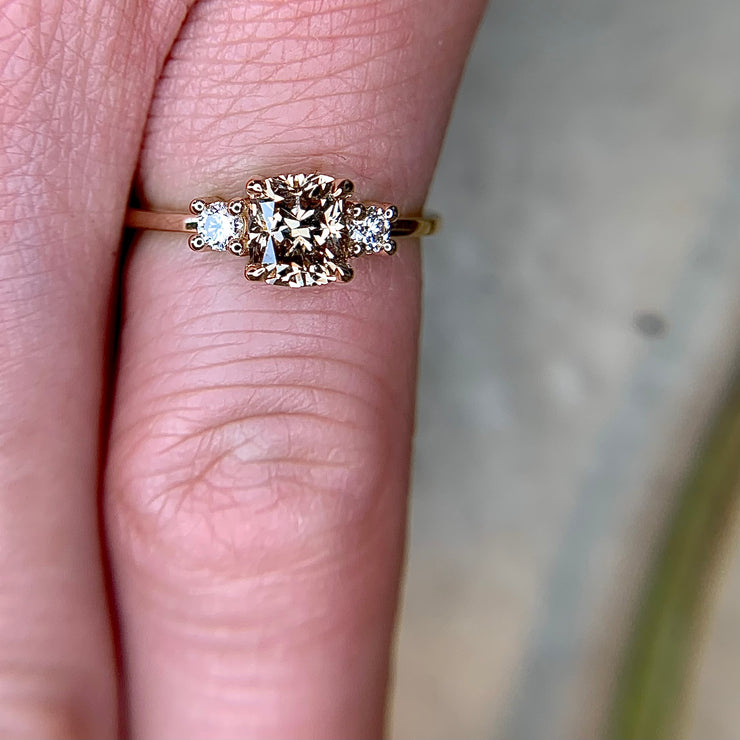 1 carat cushion champagne diamond three stone engagement ring with white diamond accents on thin gold band by Dana Walden Bridal NYC on hand